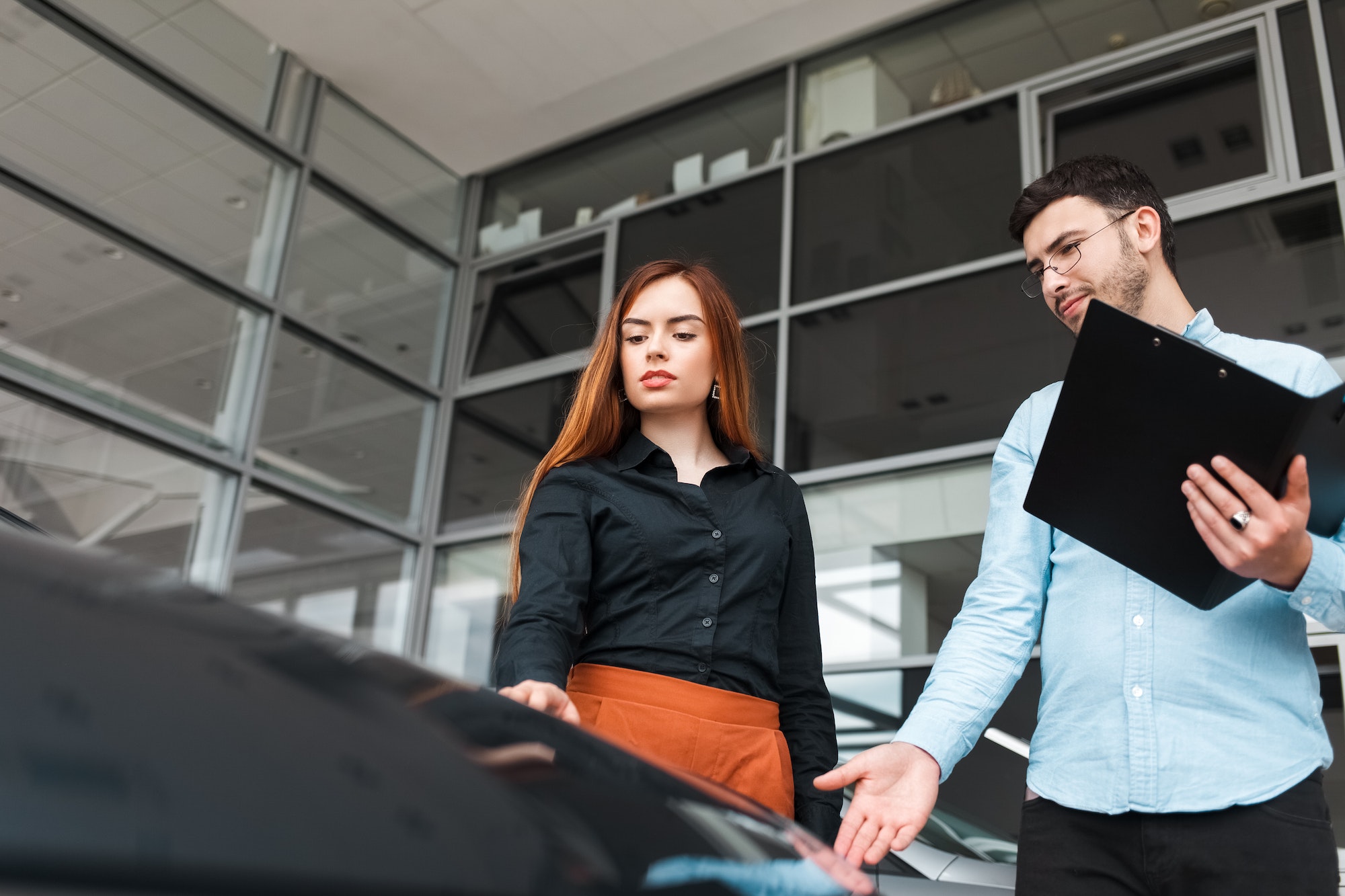 Salesman shows the car to a young client of a car dealership