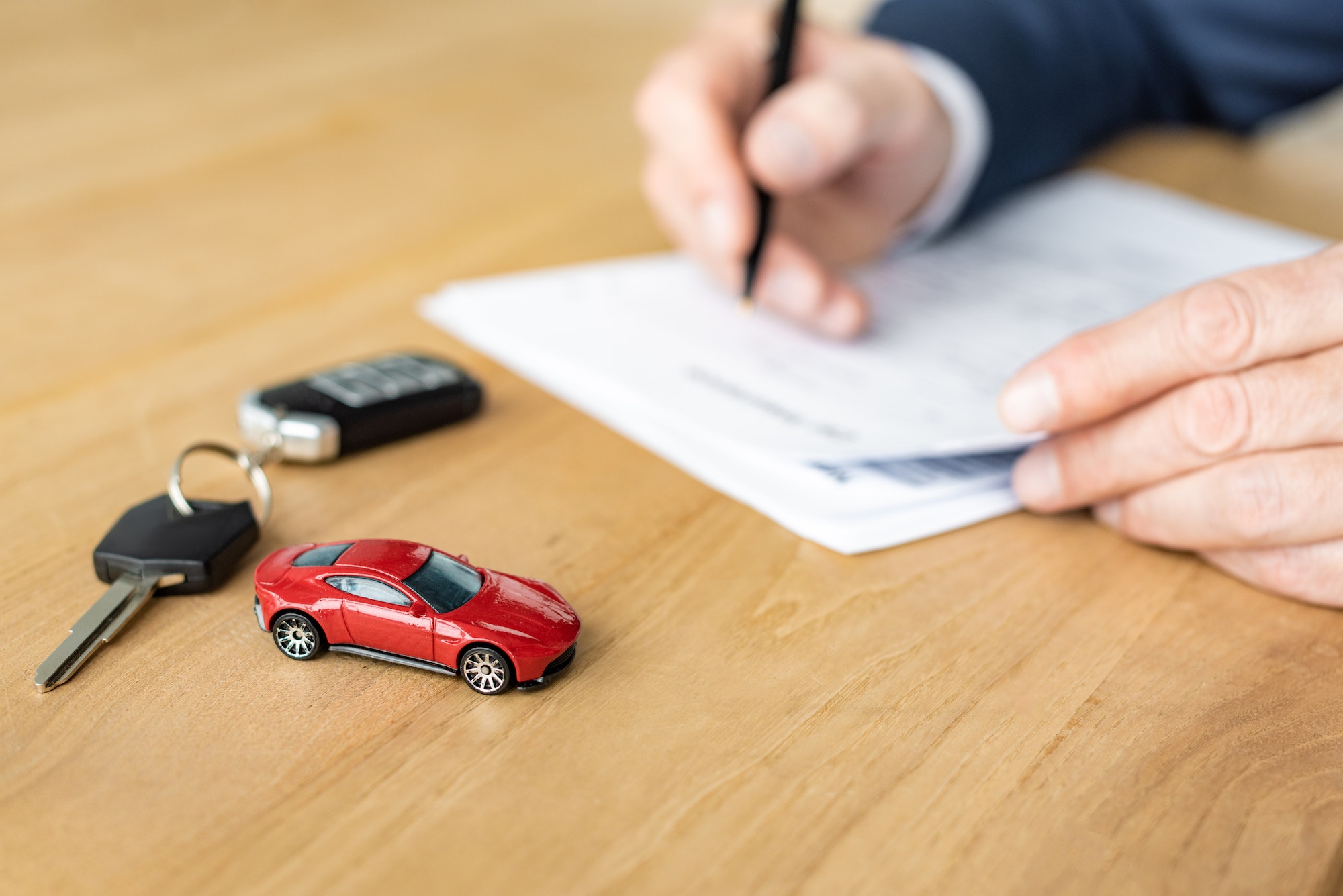 selective focus of red toy car near car key and car dealer holding pen near contract